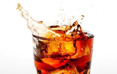 Un vaso de cola con cubitos de hielo salpicando de él.