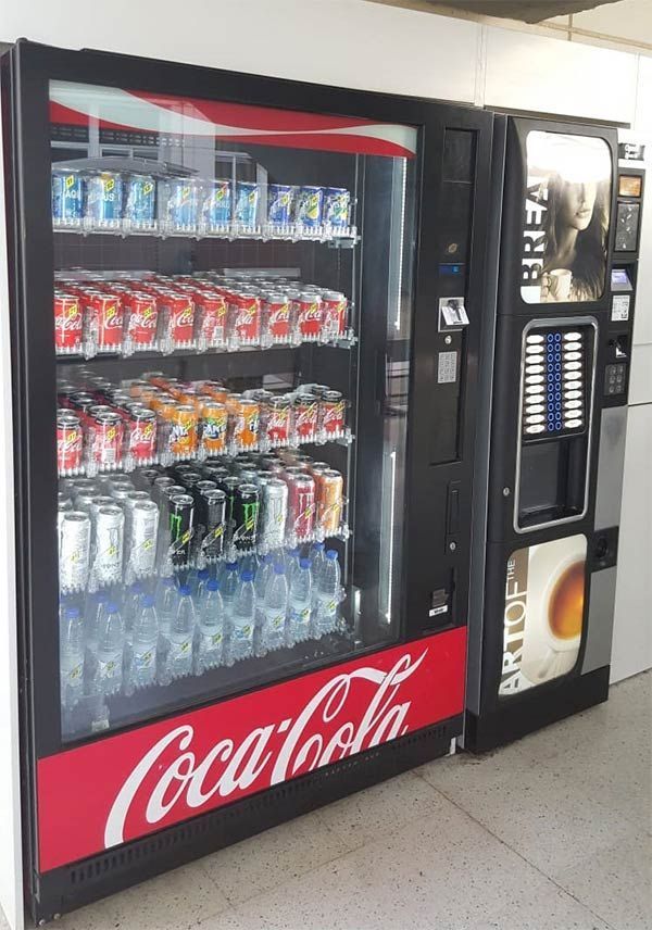 Una máquina expendedora de Coca Cola junto a una máquina expendedora de café.