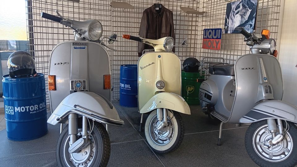Drei Vintage-Roller in einem Ausstellungsraum, grau und cremefarben, dahinter ausgestelltes Zubehör.