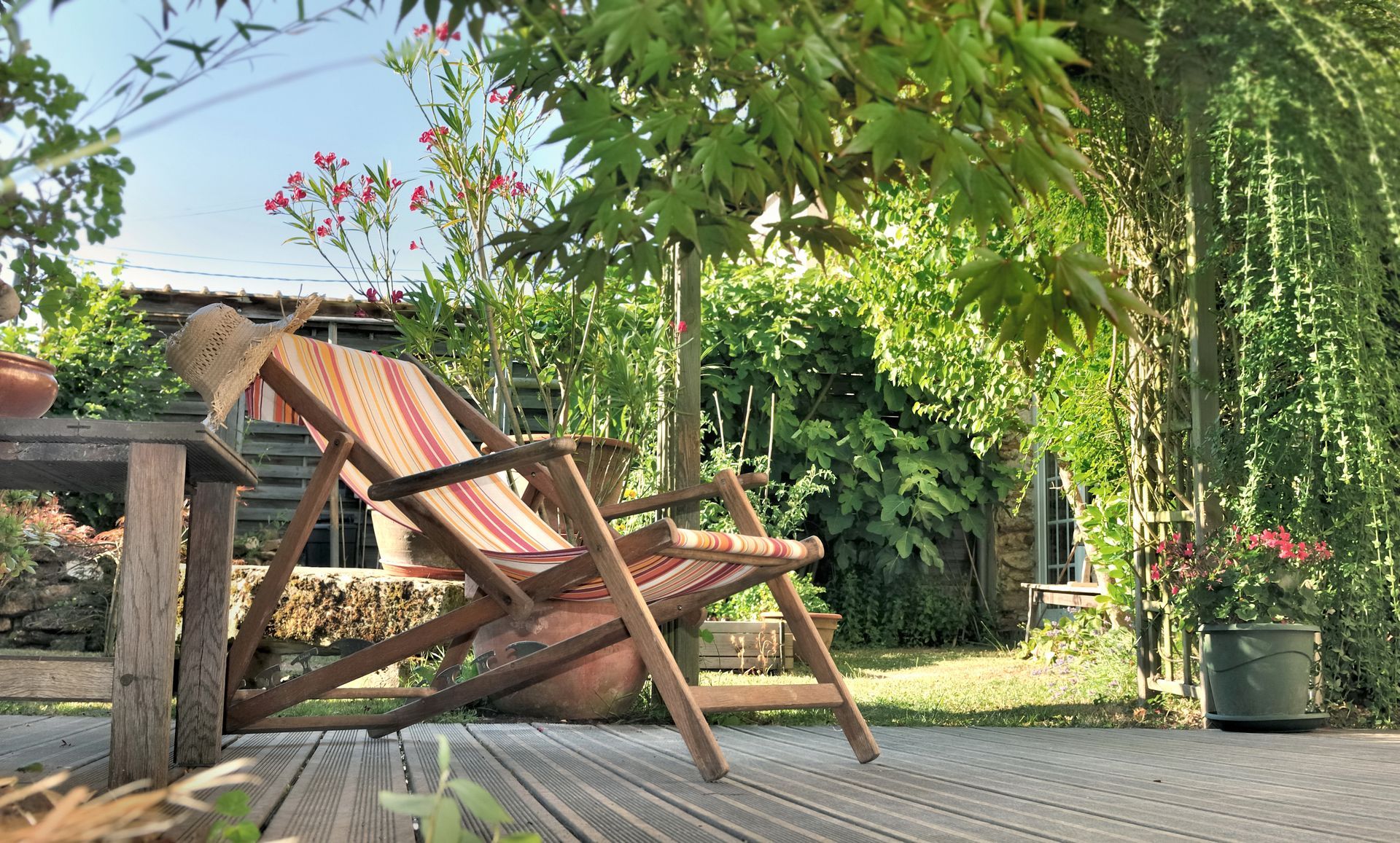 Chaises de patio en bois sur une terrasse ensoleillée, sous une végétation luxuriante composée d'arbres et de vignes grimpantes.