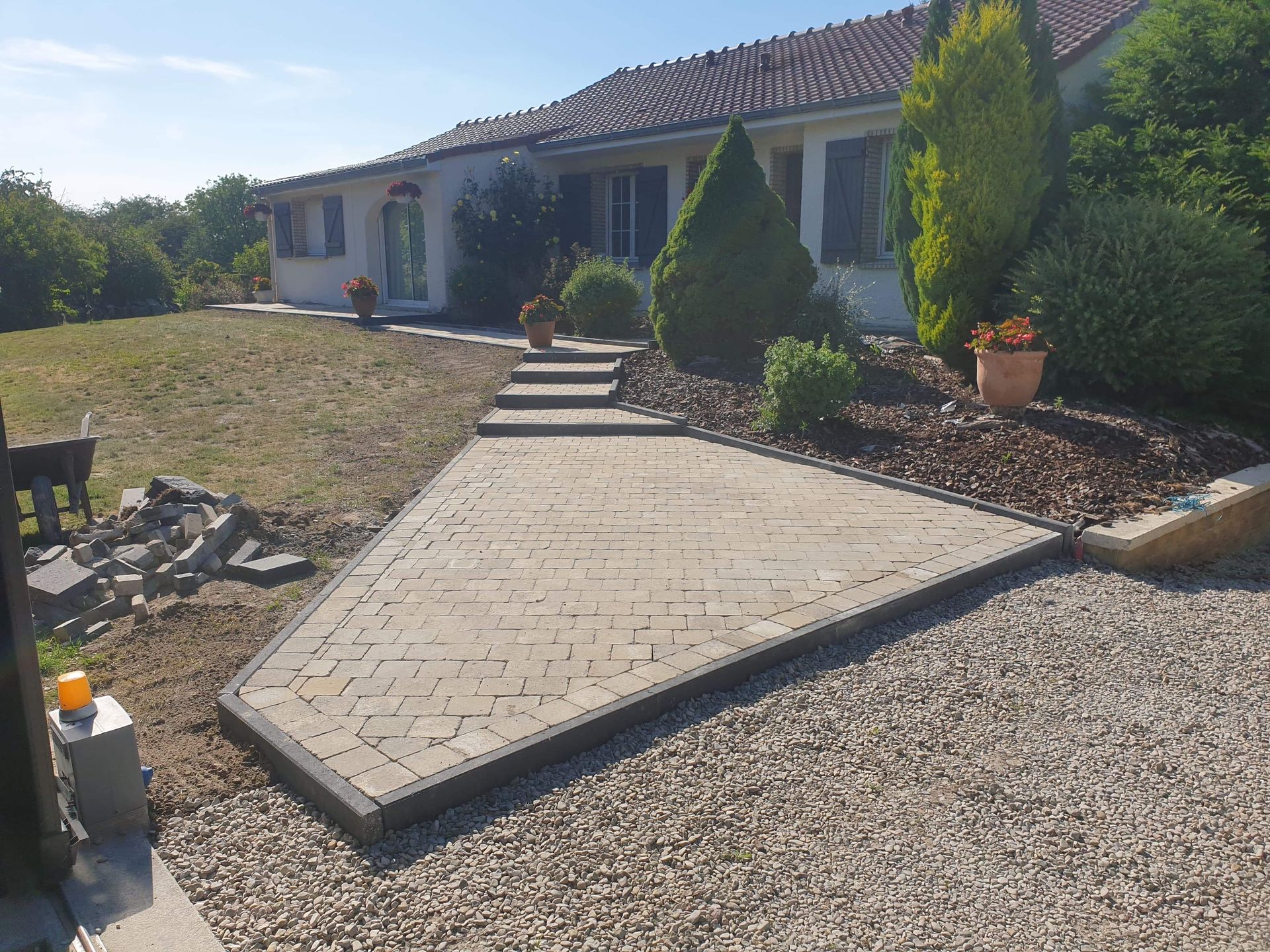 Allée menant à une maison de plain-pied avec marches, arbustes et aménagement paysager en gravier.