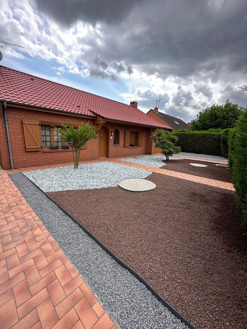 Maison en briques au toit de tuiles rouges, jouxtant un jardin paysager de gravier et de briques.