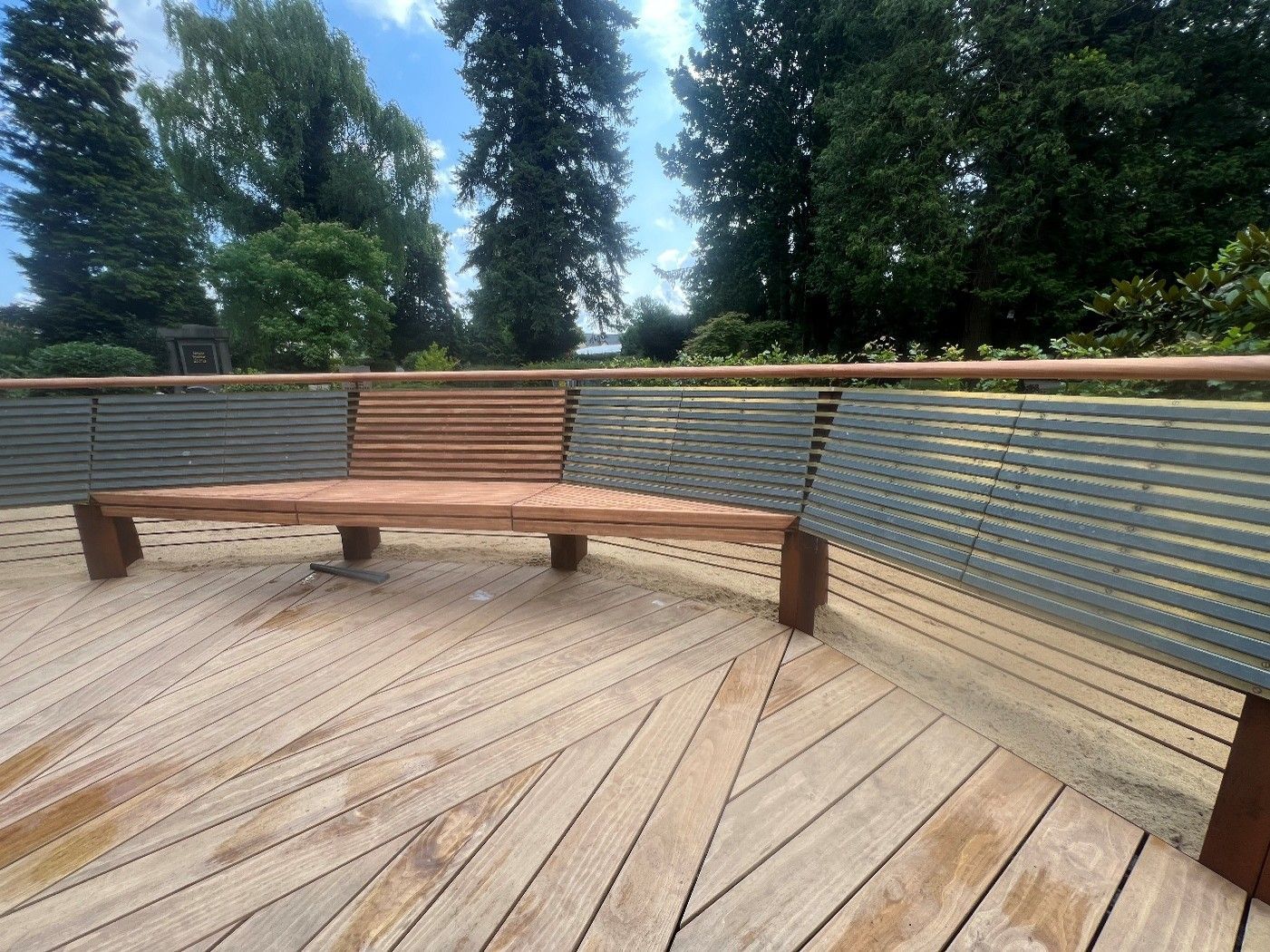 Gebogene Holzbank auf einer Terrasse mit Blick auf Bäume und blauen Himmel