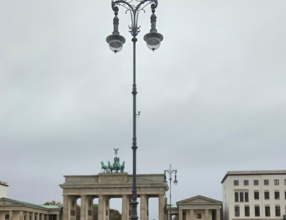 Das Brandenburger Tor in Berlin unter bewölktem Himmel, mit einer hohen Straßenlaterne im Vordergrund