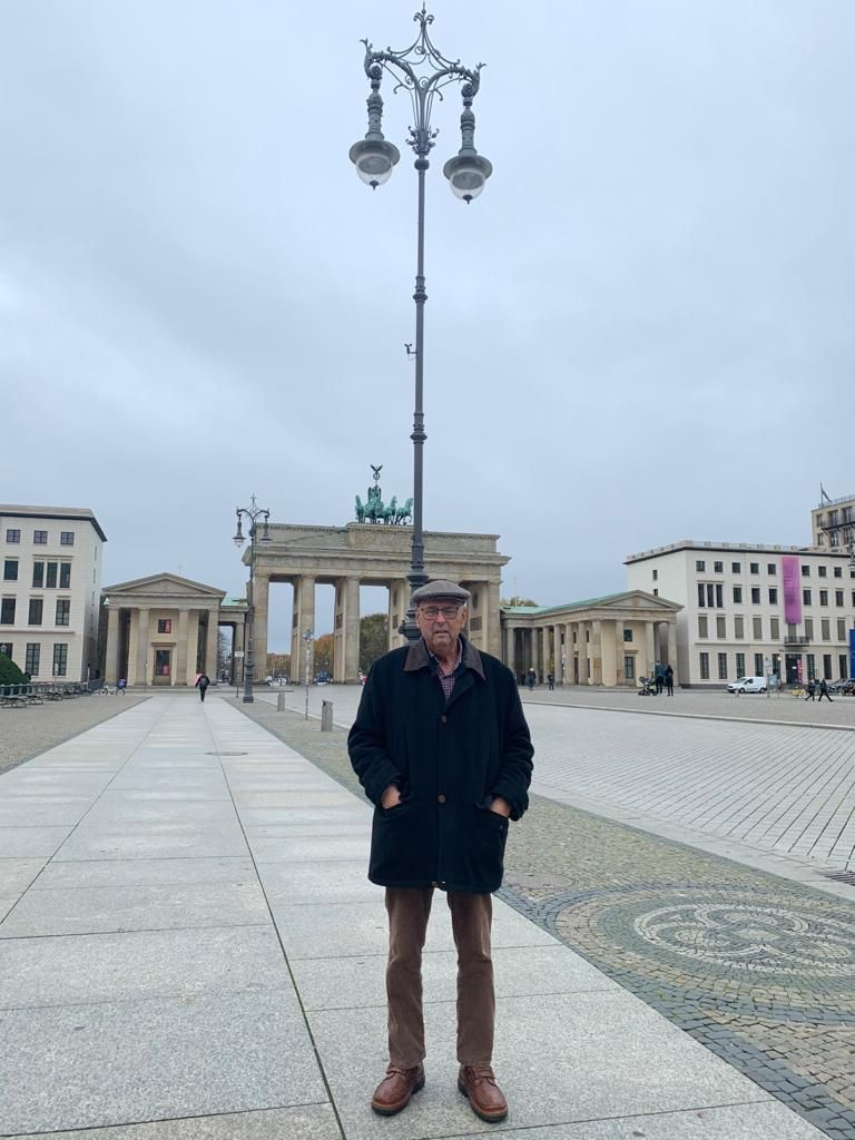Eine Person steht auf einem weiten Platz vor dem Brandenburger Tor unter einem bewölkten Himmel.