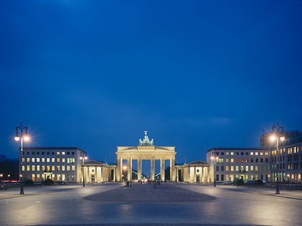 Das Brandenburger Tor, nachts vor tiefblauem Himmel beleuchtet, im Zentrum eines leeren Platzes.
