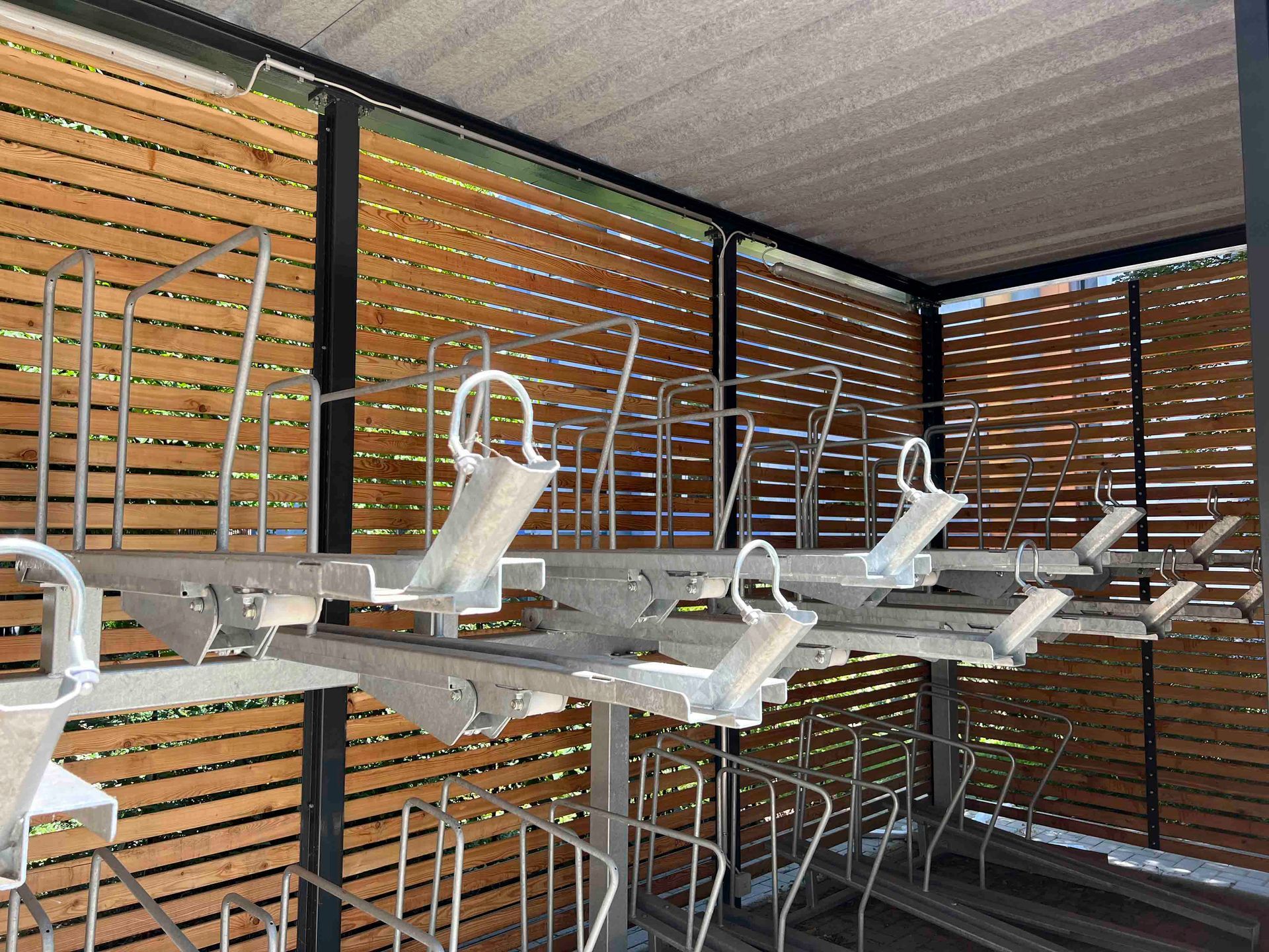 Terrasse im Freien mit leeren Metall-Esstischen und -Stühlen unter einem Lattendach und Sichtschutzwänden aus Holz.