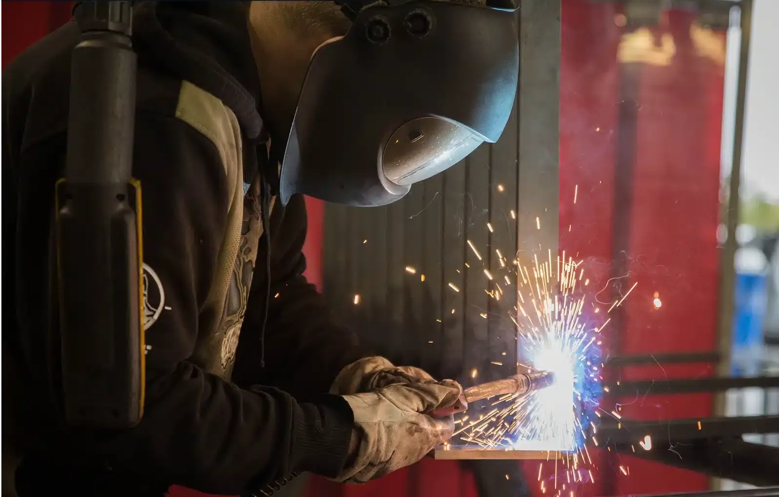 Ein Schweißer in Schutzkleidung funkt bei einer Metallbearbeitung neben einer rot glühenden Platte.