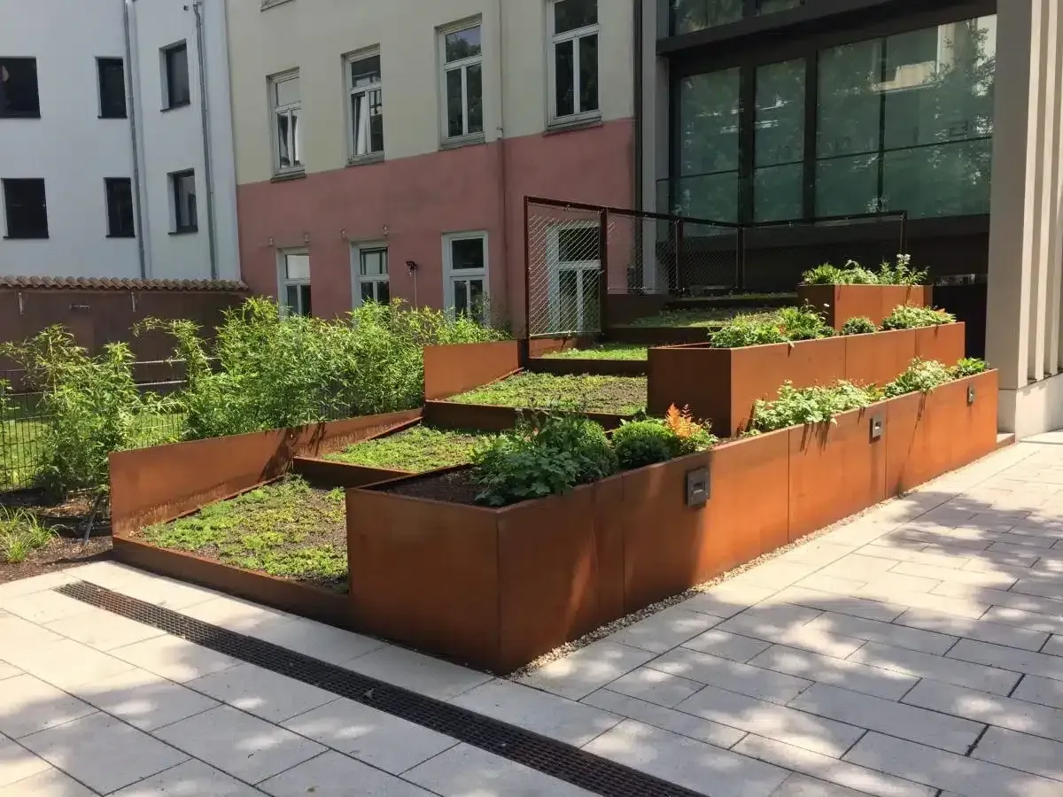 Hochbeete aus Metall mit Grünpflanzen neben einem modernen Gebäudeweg