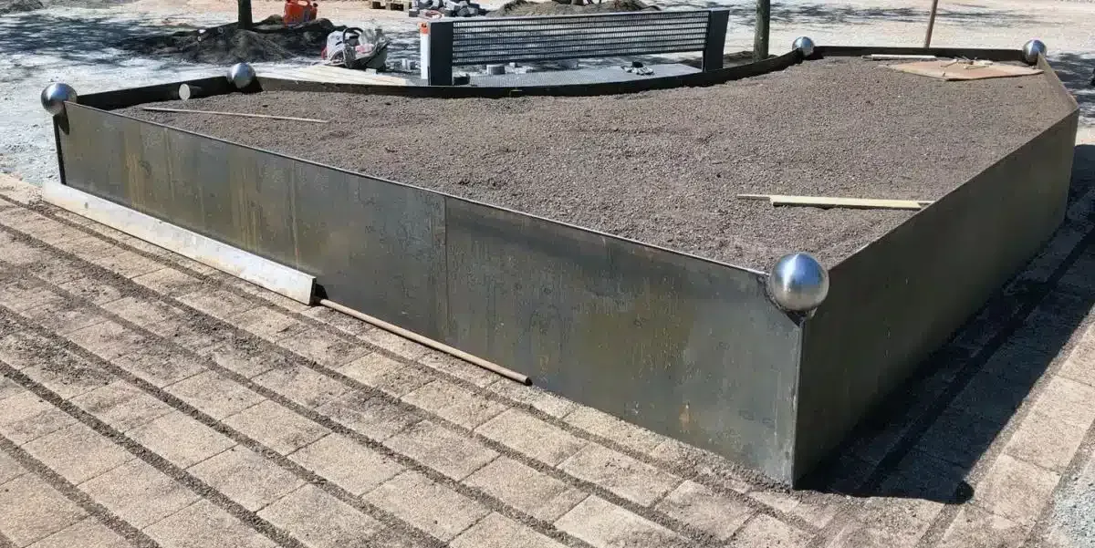Niedriges Betonpflanzbeet mit Kiesabdeckung auf einem Gehweg neben einer Straße