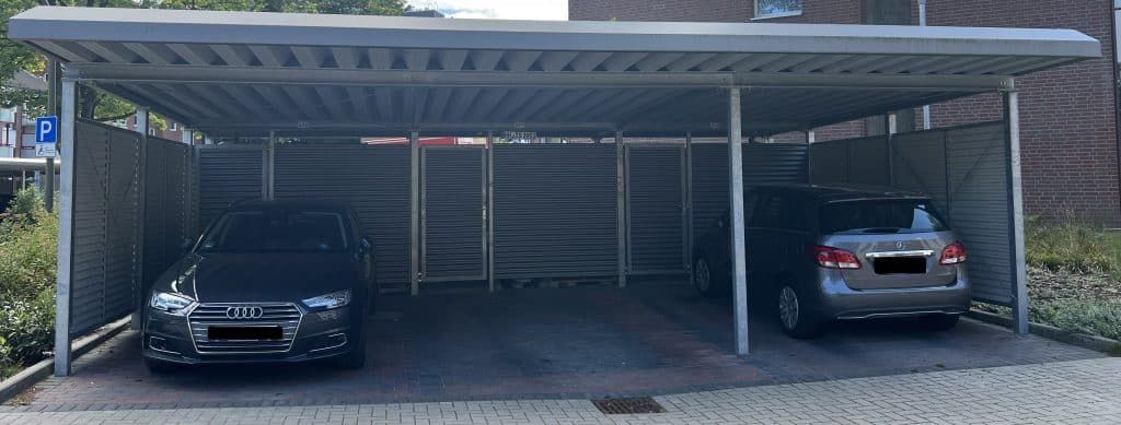 Zwei Autos parkten unter einem Carport aus Metall, eine schwarze Limousine links und ein silberner Geländewagen rechts.