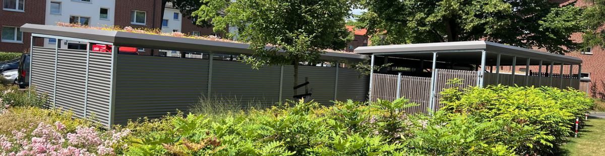 Blühende Sträucher und ein grüner Zaun neben einem Gebäude mit überdachter Terrasse in einem angelegten Garten