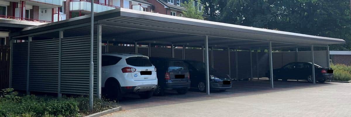 Überdachter Parkplatz mit drei geparkten Autos neben einem Gebäude und Grünflächen