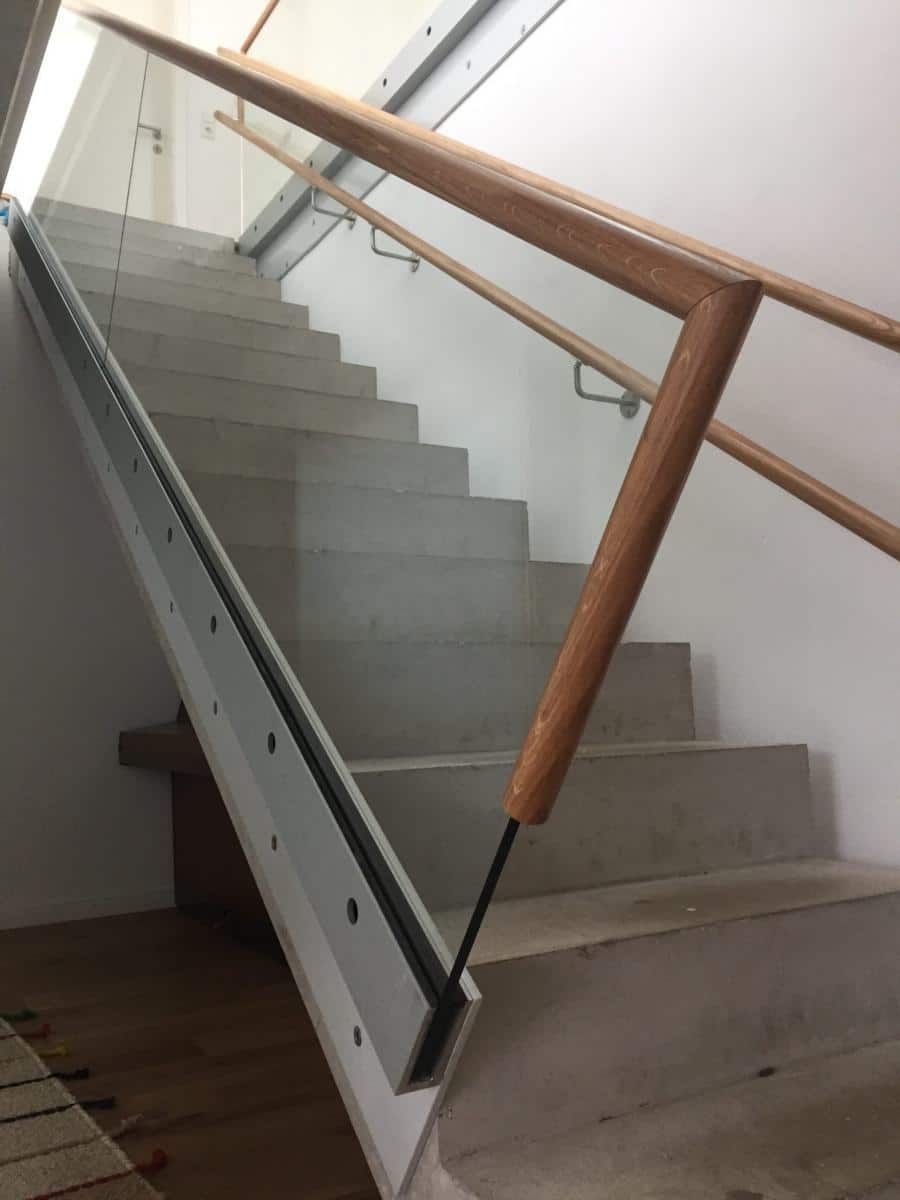 Treppenhaus mit Betonstufen und hölzernem Handlauf in einem hellen Gebäude