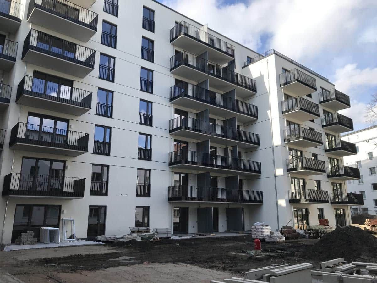 Modernes Mehrfamilienhaus mit Balkonen und Bauschutt im Vordergrund