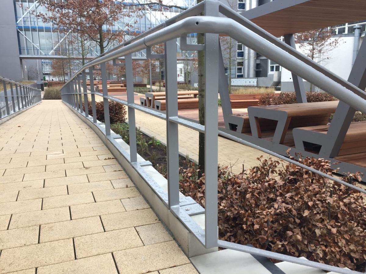 Gehweg neben einem modernen Innenhof mit Metallgeländer, Bänken und Herbstlaub