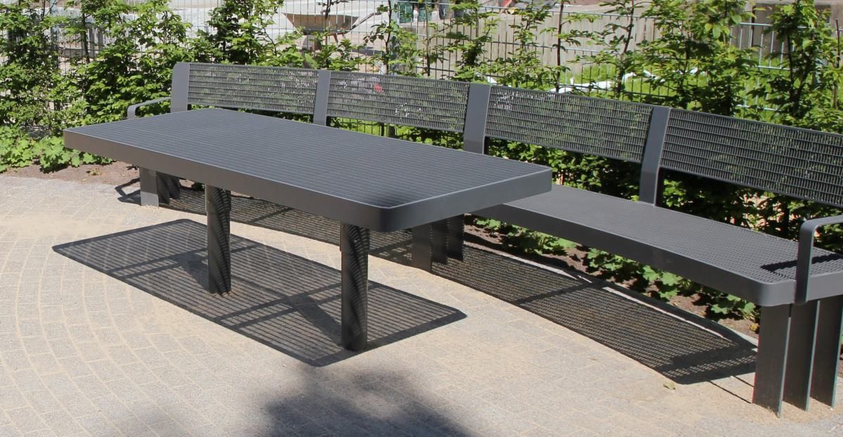 Picknicktisch und Bänke im Freien auf einer gepflasterten Terrasse neben Grünflächen.