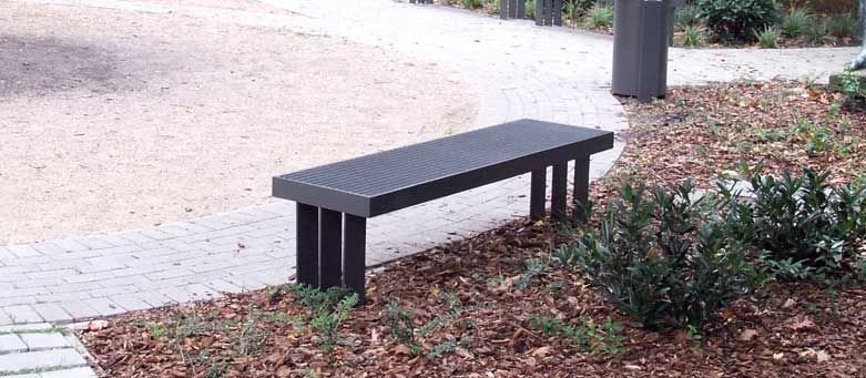 Lange schwarze Bank neben einem Backsteinweg und einem mit Sträuchern bewachsenen Mulchbeet.
