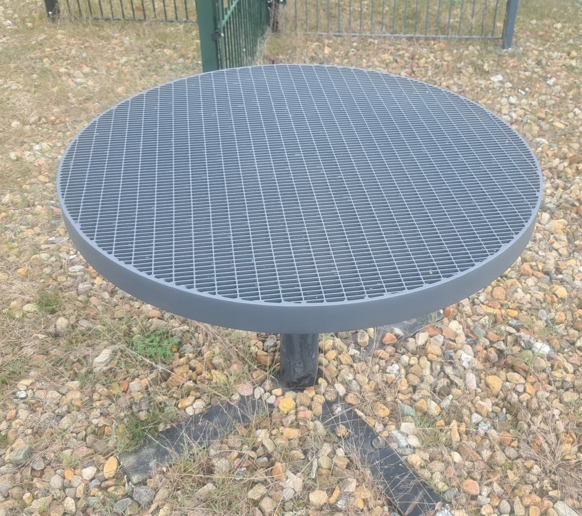 Runder schwarzer Metall-Gartentisch auf Kies, mit einem wirbelnden Gittermuster auf der Tischplatte.