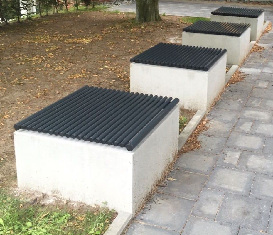 Weiße Betonbänke mit schwarzen gerippten Oberflächen entlang eines gepflasterten Weges in einem Park