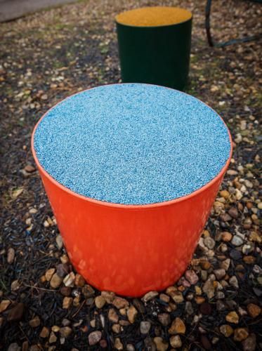 Drei bunte, zylindrische Behälter auf Kieselsteinen: orange, grün und gelb mit Deckel.