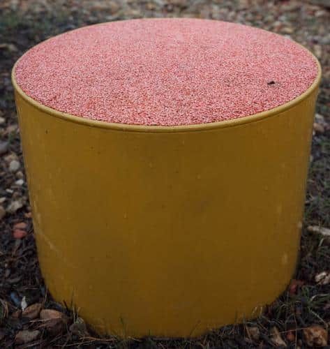 Gelber zylindrischer Behälter mit rosa gesprenkeltem Deckel im Freien auf dem Boden