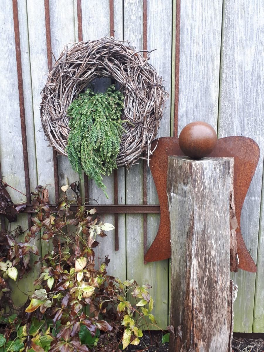 Rustikale Gartenmauer mit einem Zweigkranz und grünem Laub neben einem verwitterten Pfosten
