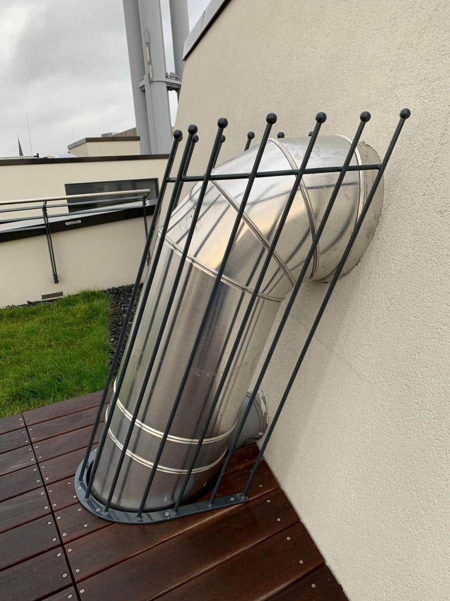 Metallene Terrassenstühle, seitlich an eine Wand auf einer Holzterrasse neben einem Balkongeländer gestapelt.