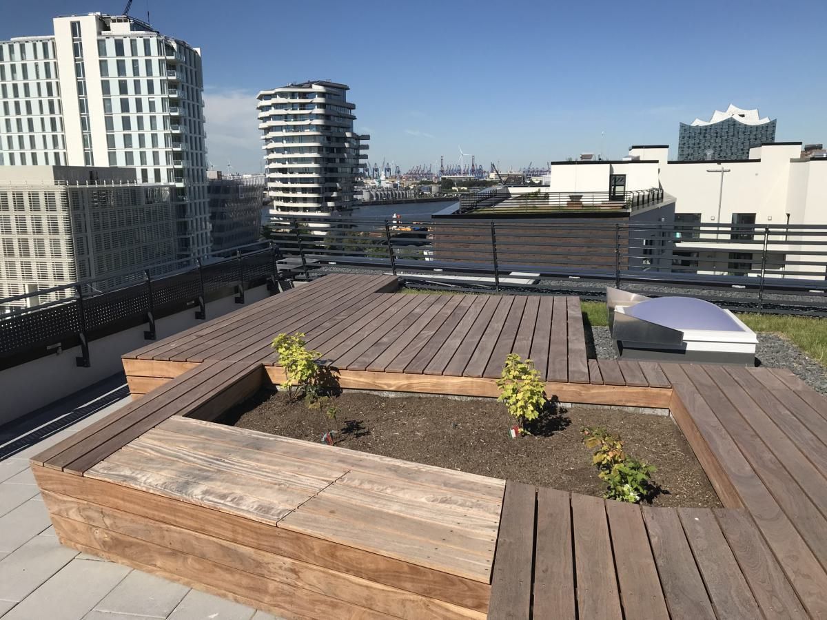 Dachterrasse mit Holzdeck, Pflanzkästen und Stadtgebäuden im Hintergrund