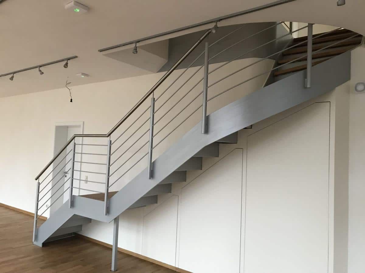 Geschwungene, graue Metalltreppe mit Geländer in einem hellen, modernen Interieur