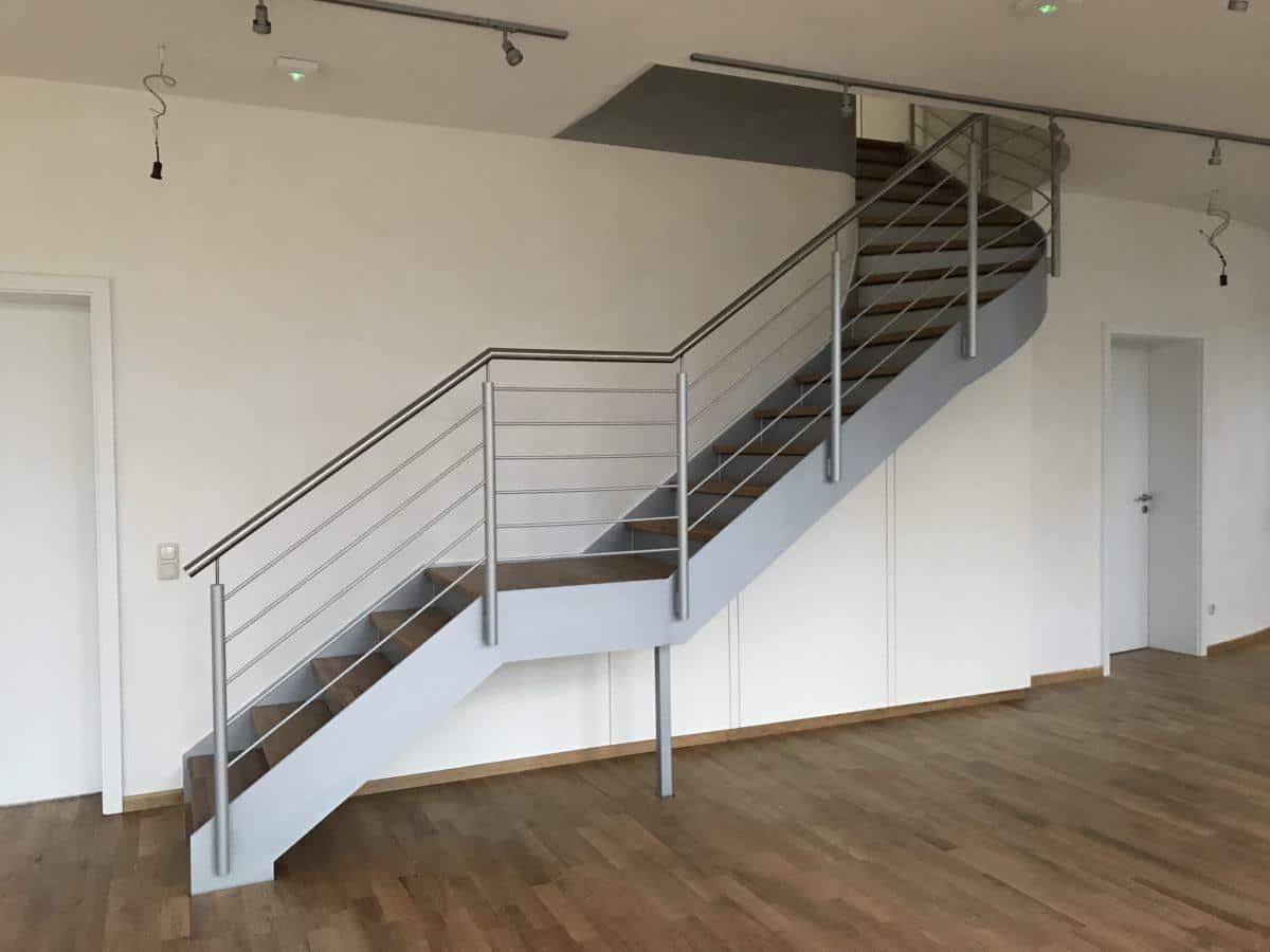 Innentreppe mit Metallgeländer in einem spärlich möblierten Zimmer mit Holzboden