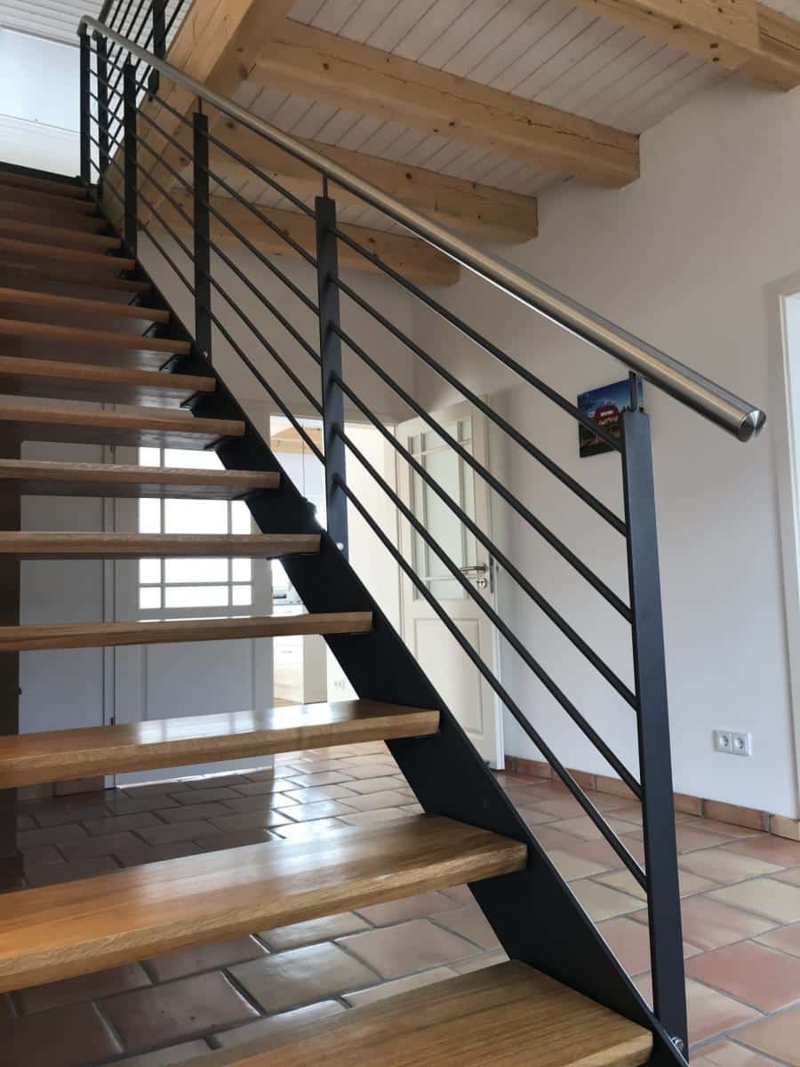 Moderne Innentreppe mit Holzstufen, schwarzem Metallgeländer und weißen Wänden unter freiliegenden Balken