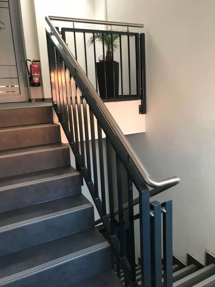 Innentreppenhaus mit schwarzem Metallgeländer und einer Topfpflanze auf dem Treppenabsatz