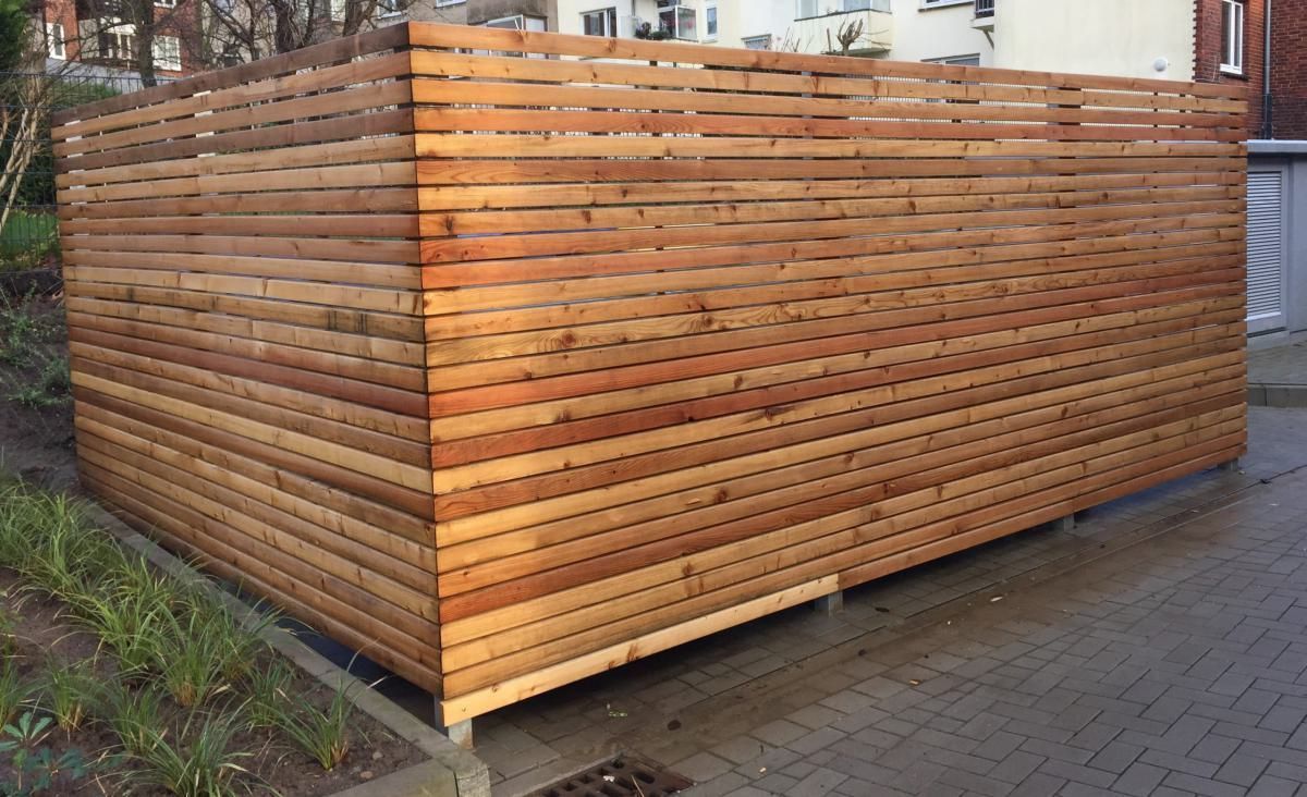 Ein hölzerner Lattenzaun umschließt eine Ecke eines Gehwegs neben einem Gebäude.