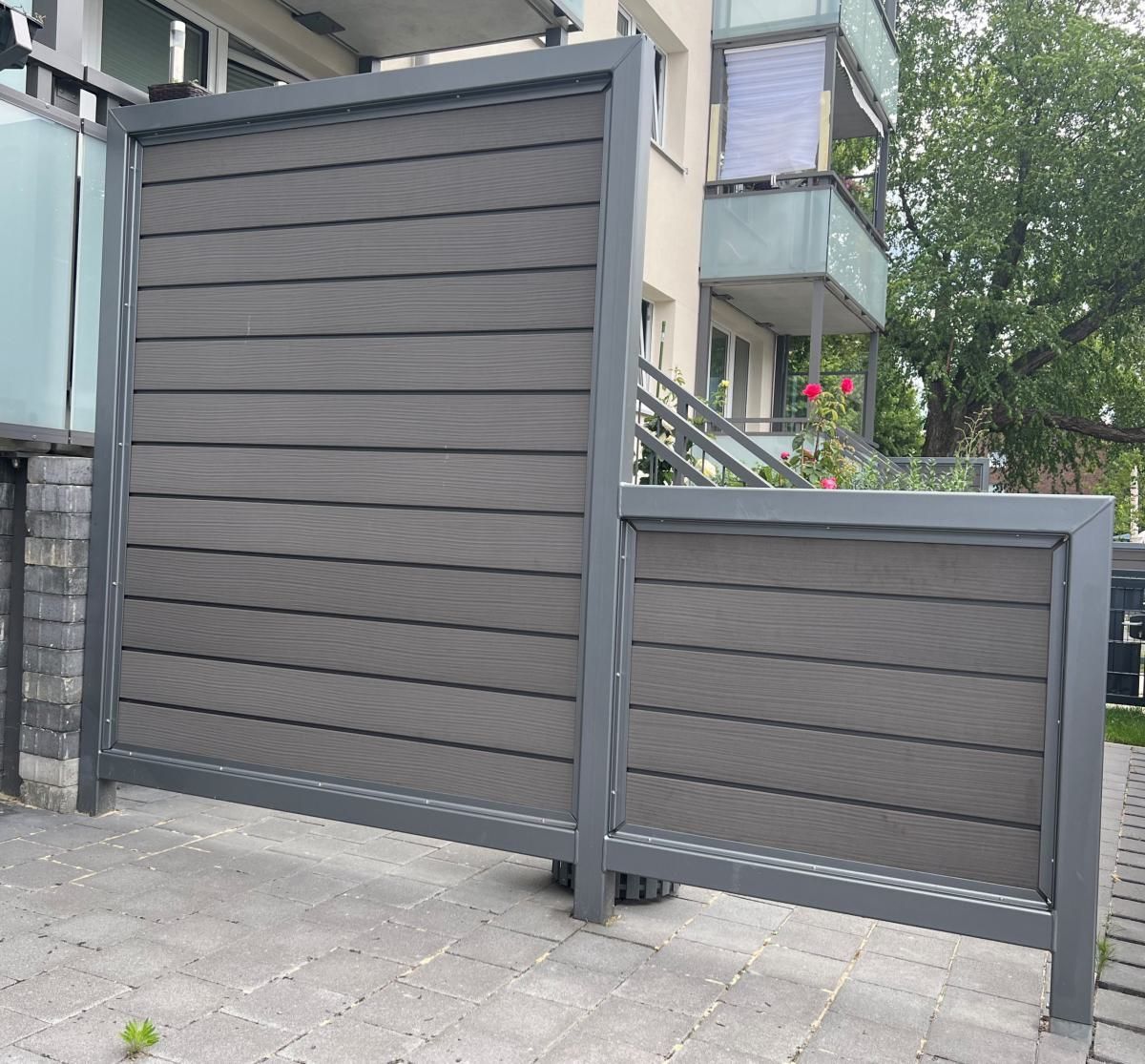 Graue Lattenzaunpaneele neben einer Einfahrt vor einem Mehrfamilienhaus