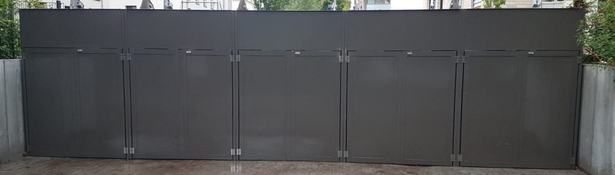 Großes, dunkelgraues Metalltor mit mehreren Paneelen vor einer Betonmauer.