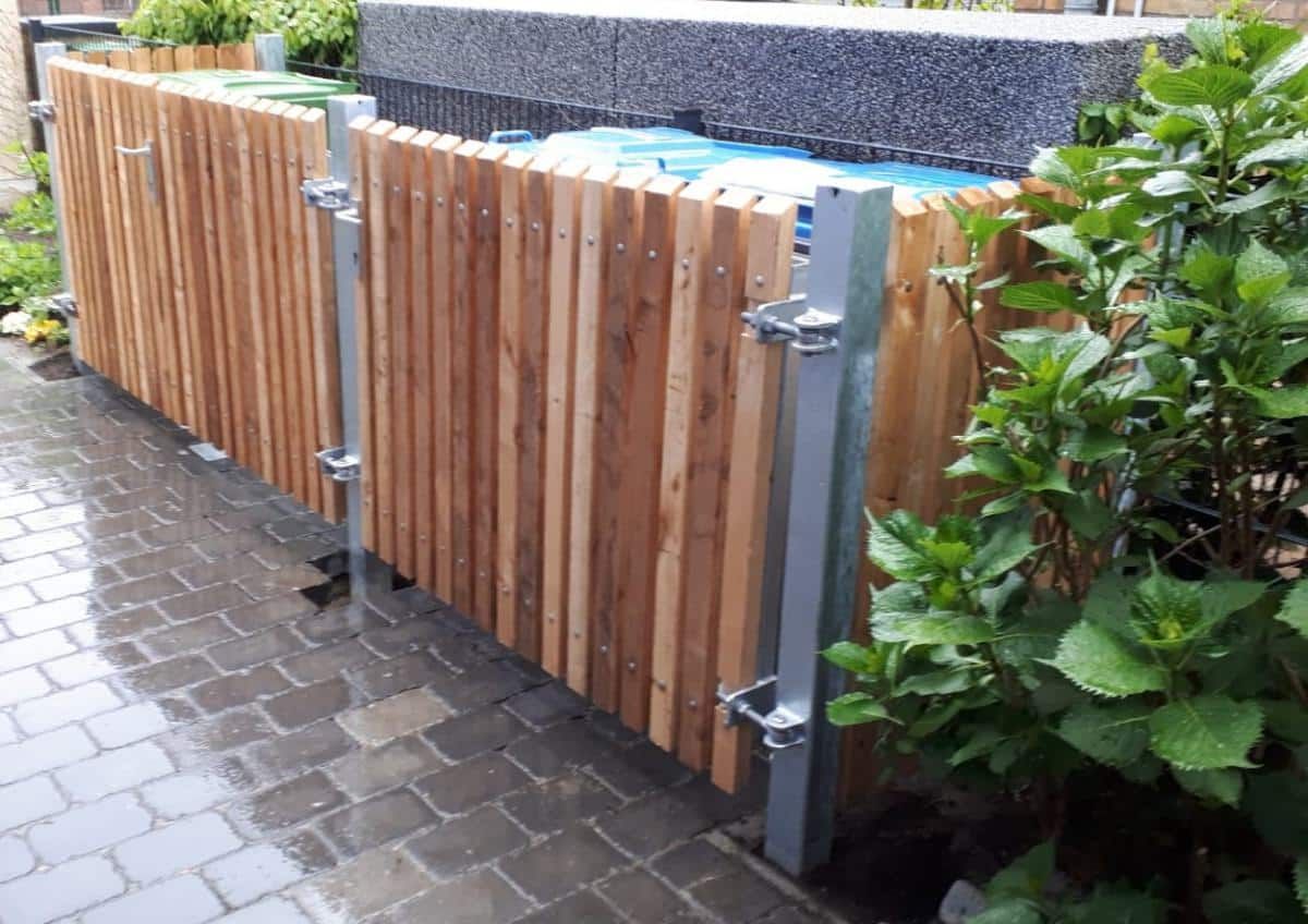 Schwingtor aus Holz mit Metallpfosten neben einem gepflasterten Gehweg und grünen Sträuchern
