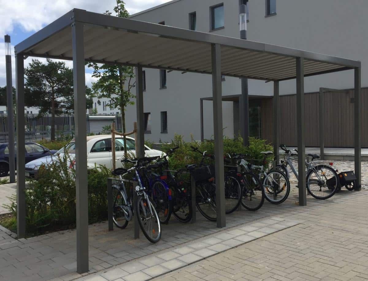 Fahrräder sind unter einem metallenen Fahrradunterstand neben einem Bürogebäude und dem Gehweg geparkt.