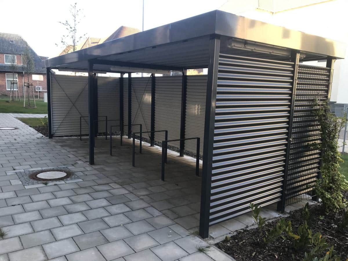 Überdachter Fahrradunterstand mit Metallrahmen und Lattenwänden auf einem gepflasterten Innenhof