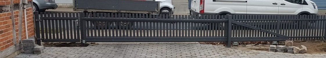 Schwarzes Metallgeländer mit drei Bänken auf einem Gehweg neben geparkten Autos und einer Straße