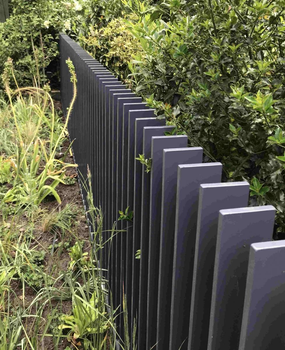 Schwarzer Metallzaun neben dichtem, grünem Gebüsch und hohem Gras