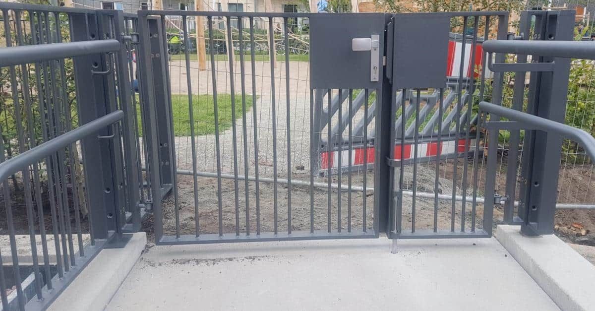 Schwarzes Metalltor an einem Gehwegeingang mit einem Tastenfeld und einer rot-weißen Absperrung dahinter