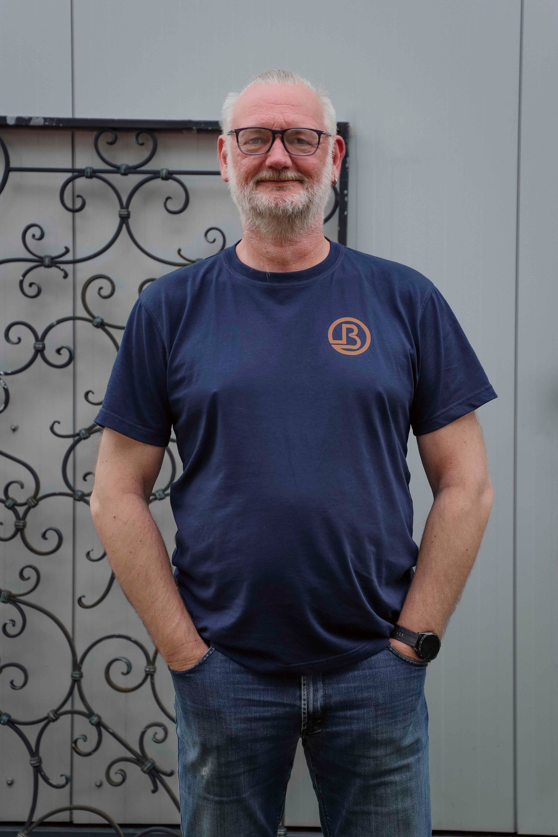 Ein Mann in einem dunkelblauen T-Shirt und Jeans steht lächelnd mit den Händen in den Hosentaschen