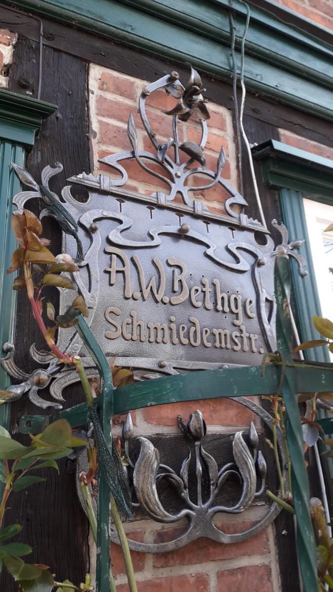 Verwittertes, hängendes Ladenschild an einem Backsteingebäude mit kunstvollen schwarzen Eisenbeschlägen 