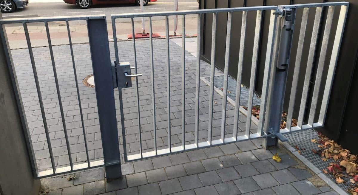 Ein geschlossenes graues Metalltor versperrt den Eingang zu einem gepflasterten Gehweg