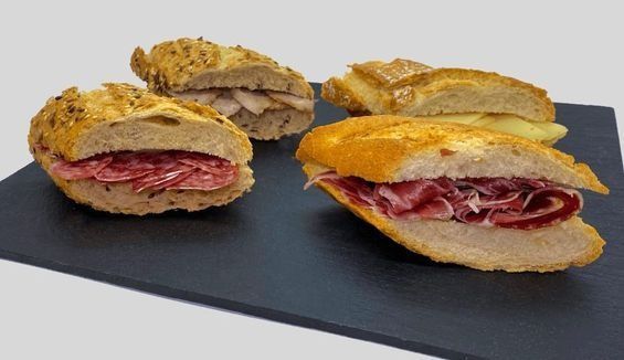Hay tres sándwiches sobre una tabla de cortar negra.