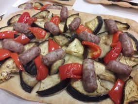 Una pizza con berenjenas, pimientos y salchichas sobre una mesa.