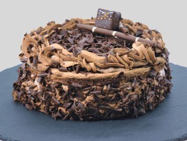Un pastel de chocolate con virutas de chocolate encima está sobre un plato negro.