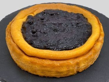 Un primer plano de una tarta de queso con salsa de arándanos en un plato negro.