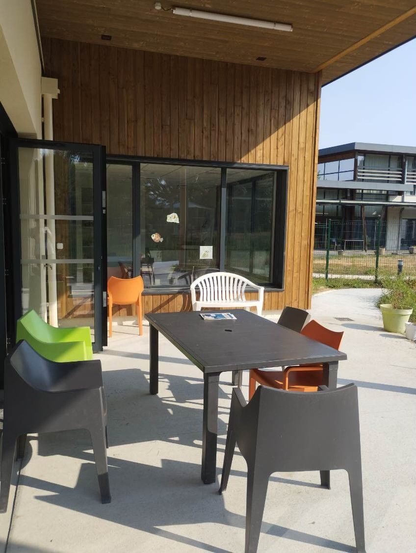 Terrasse extérieure avec chaises noires, table et portes coulissantes en verre à côté d'un bâtiment en bois